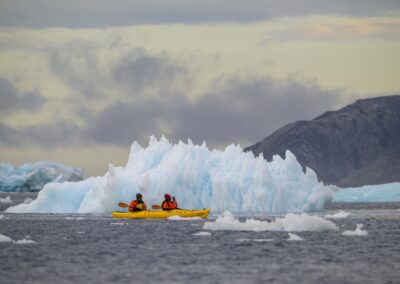 Kayakers kayaking in front of iceberg